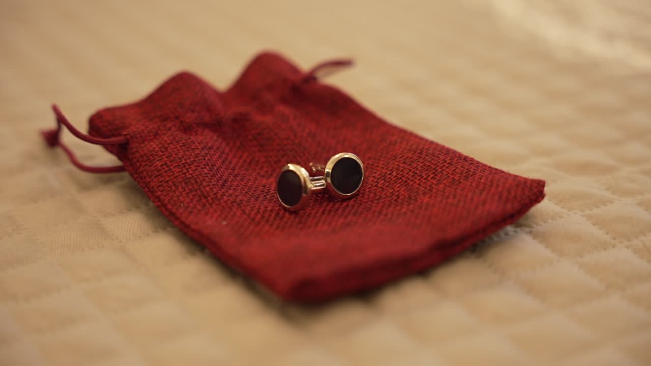 베이지색 트 된 표면에 빨간색 직물 가방에 배치 된 우아한 cufflinks의 근접