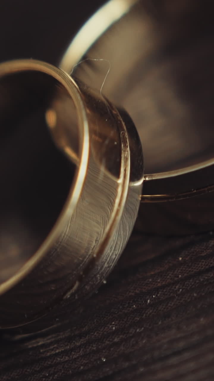 Pair of elegant gold wedding rings on black wooden surface extreme closeup slow motion. Accessories for bride and groom. Jewelry for wedding ceremony