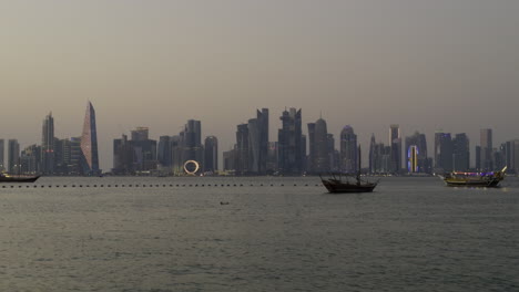 doha skyline at sunset, featuring modern skyscrapers along the waterfront, with boats in the foreground as sunset glow spreads across sky on multi colored buildings