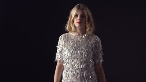 blonde woman in sparkly dress walking to camera, into focus