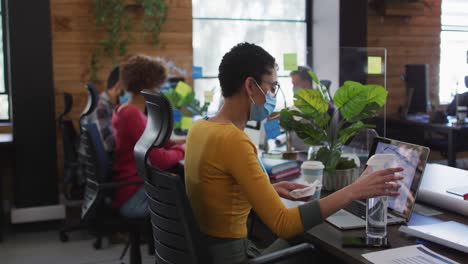 mujer caucásica con máscara limpiando su computadora portátil usando pañuelo y spray desinfectante en un moderno