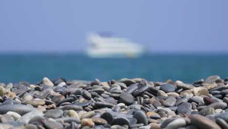 pebbles on sunny beach with blurry ship at sea zooming out