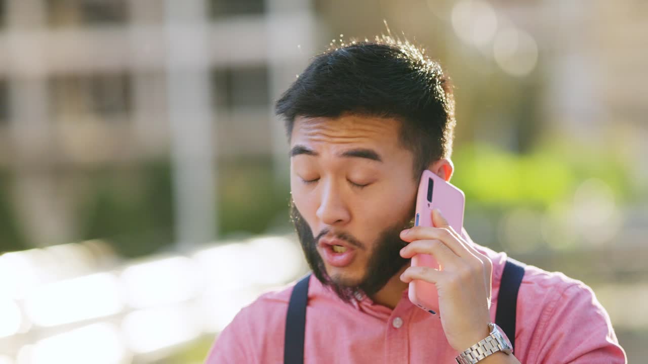 Young Asian man talking on a pink smartphone outdoors