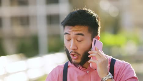 young asian man talking on a pink smartphone outdoors