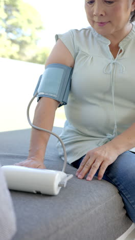 vertical video: measuring blood pressure, woman using digital monitor at home, focusing on health