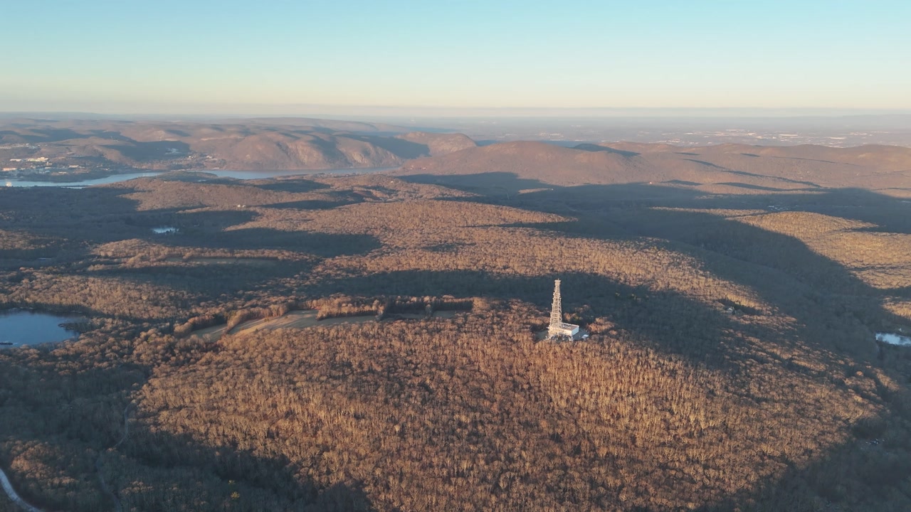 Beautiful aerial footage flying over a vast autumn forest with rolling hills and a solitary radio tower bathed in the warm light of sunrise, with a river visible in the distant valley