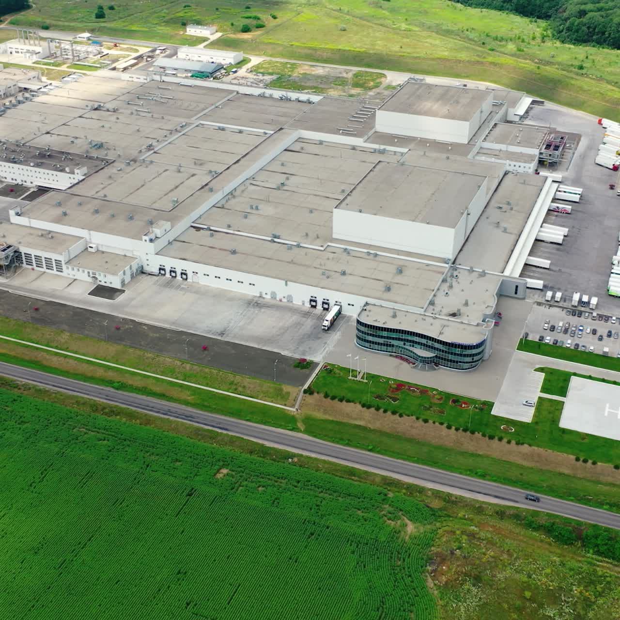 Factory on green field. Exterior of a modern industrial plant. White trucks and cars are on parking spaces. Aerial view