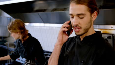Chef-looking-at-clipboard-while-talking-on-mobile-phone-4k