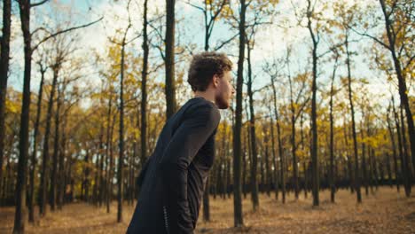 un hombre serio con cabello rizado con barba en un uniforme deportivo negro mira su reloj, anota la hora y comienza su carrera en el bosque de otoño por la mañana