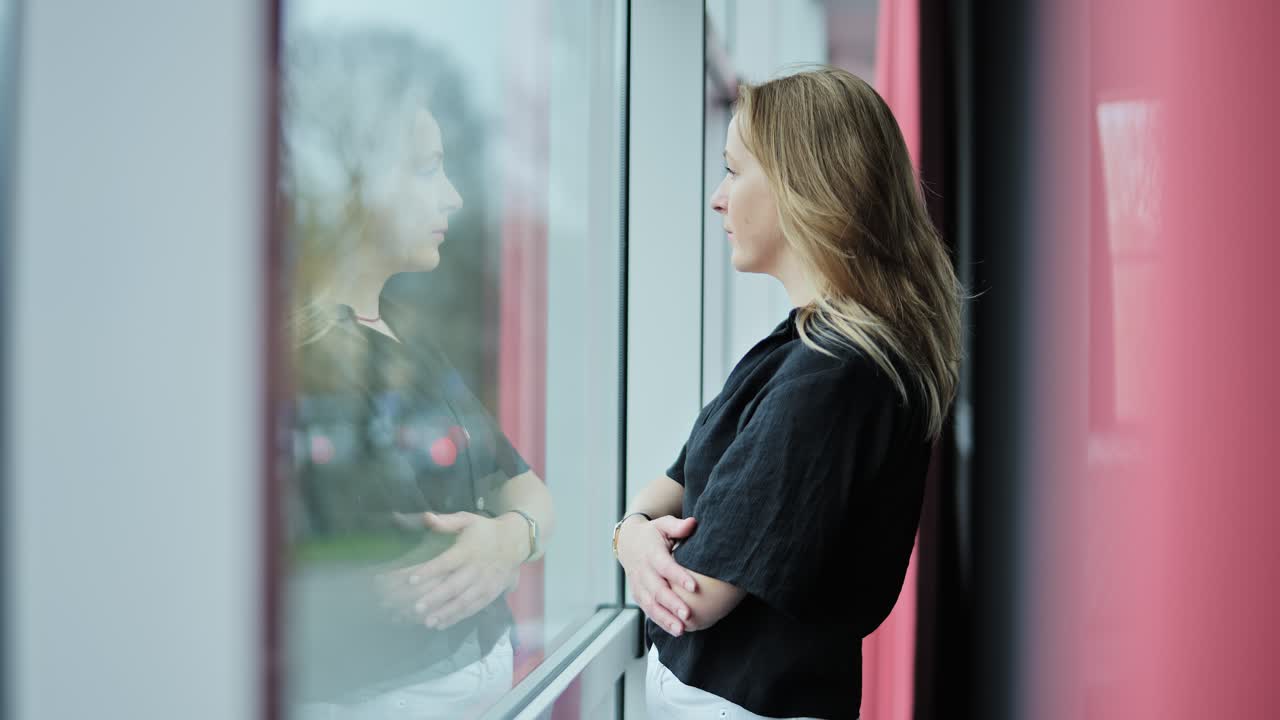 Mujer de negocios deprimida de pie cerca de un cristal, mirando hacia afuera a la luz del día