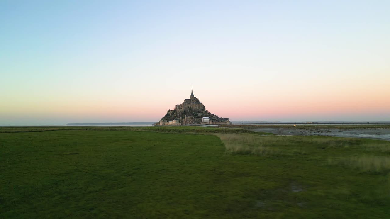 vista aérea de un avión no tripulado del monte saint-michel volando sobre la hierba de izquierda a derecha al atardecer