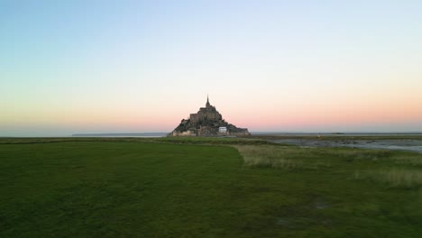 aerial drone view of mont saint-michel flying over grass from left to right at sunset