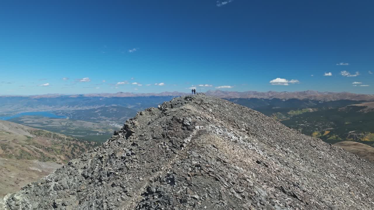 Drone dolly along ridgeline to two hikers at the top of Peak 10 Trail in Breckenridge, enjoying the panoramic mountain views