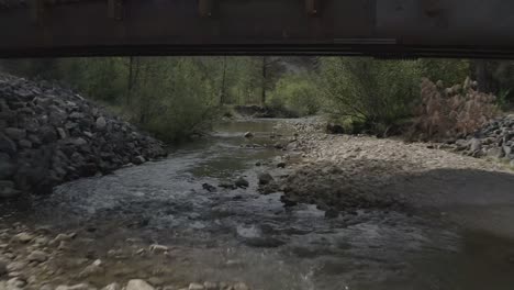 aerial drone shot of a fast fly under bridge over creek