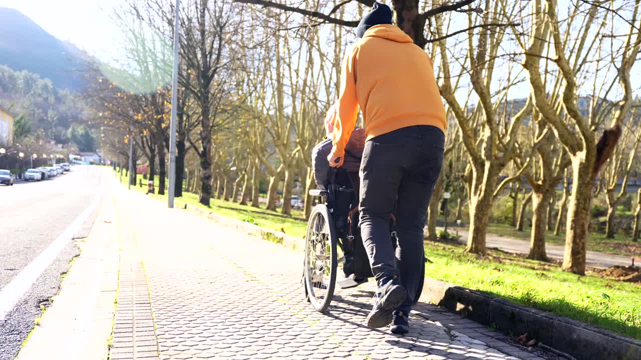 A man pushing a wheelchair on a sidewalk in autumn