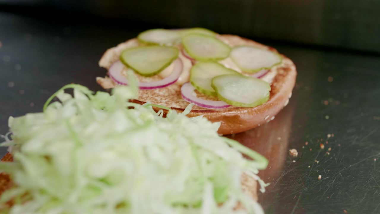 pepinillos y lechuga en hamburguesas que se ponen juntos en la cocina, primer plano