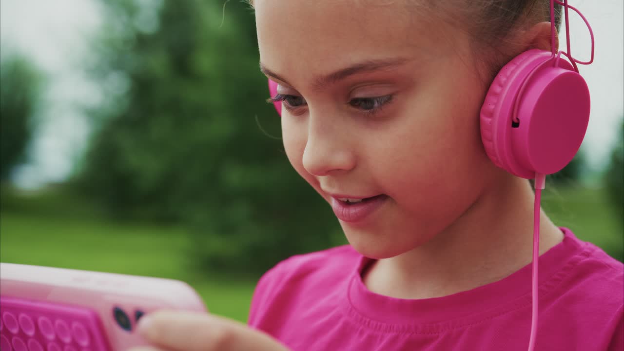 A Young Girl Enjoying Music with Pink Headphones While Engaged with Her Smartphone in a Scenic Outdoor Setting Amidst Lush Greenery