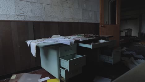 slider footage of an abandoned desk covered in papers with open drawers in an abandoned factory office