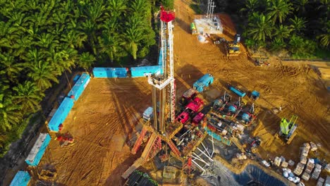 Cinematic-4K-Drone-Footage-of-Onshore-Drilling-Rig-equipment-structure-for-oil-exploration-and-exploitation-in-the-middle-of-jungle-surrounded-by-palm-oil-trees-during-sunset-and-high-oil-price