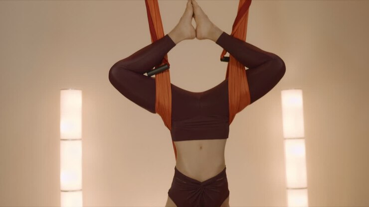 Woman practicing inverted butterfly pose in hammock. Lady doing antigravity yoga