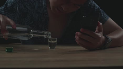 close up of drunk, depressed asian man drinking vodka from glass during using smartphone in black background