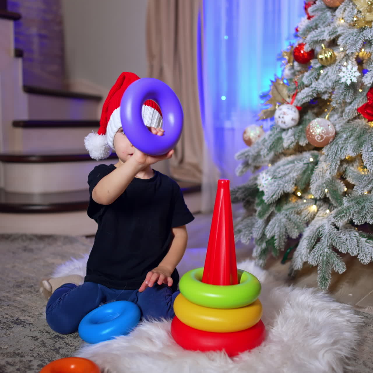 Two year old toddler in Santa cap plays with pyramid. Lovely child having fun at home at Christmas.