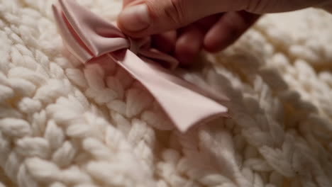 a hand touching a pink ribbon bow on a white knitted blanket