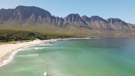 dynamic aerial shot of green can calm sea and big mountain formation in the background near cape town