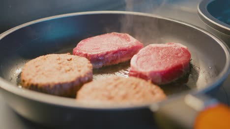 close up - cooking two vegan burgers and two steaks in a pan with olive oil