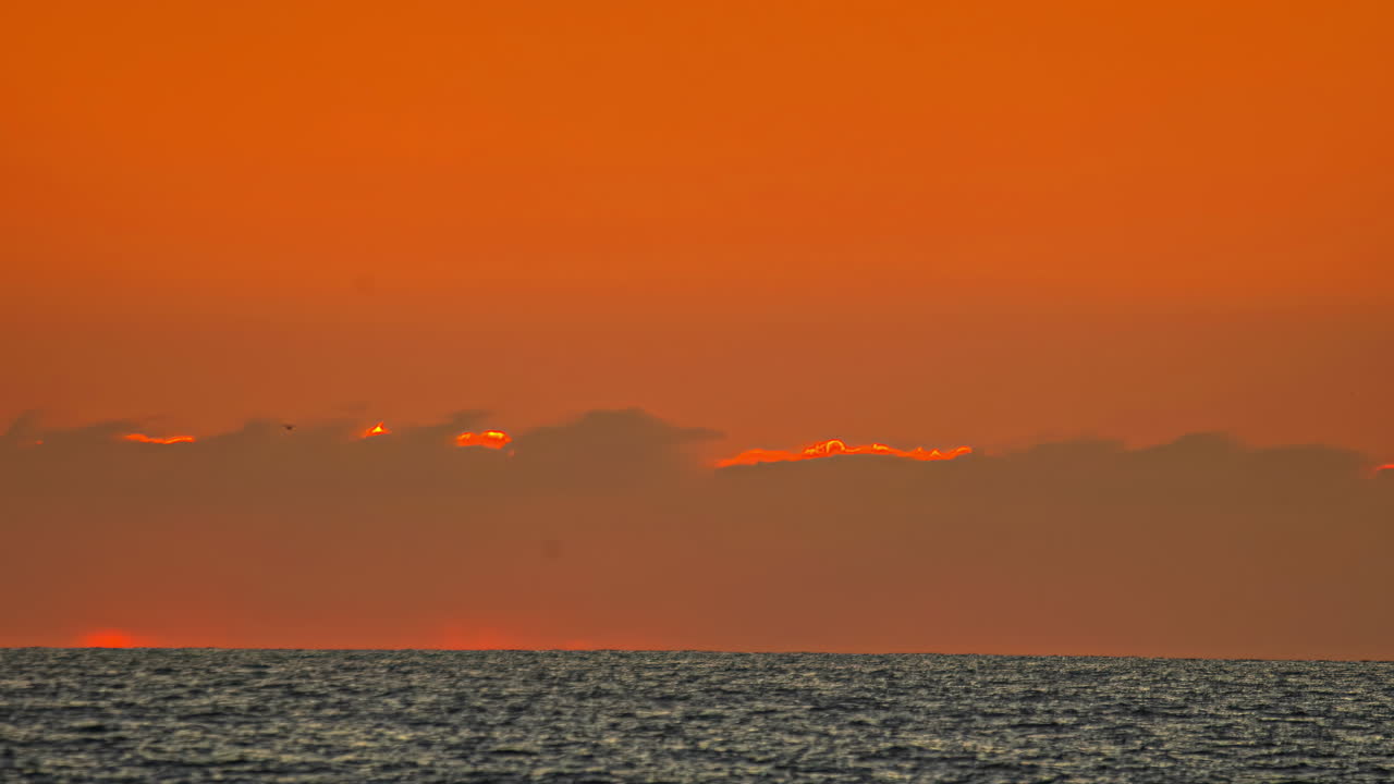 Sun rising behind a cloud on the horizon of the sea. Time lapse