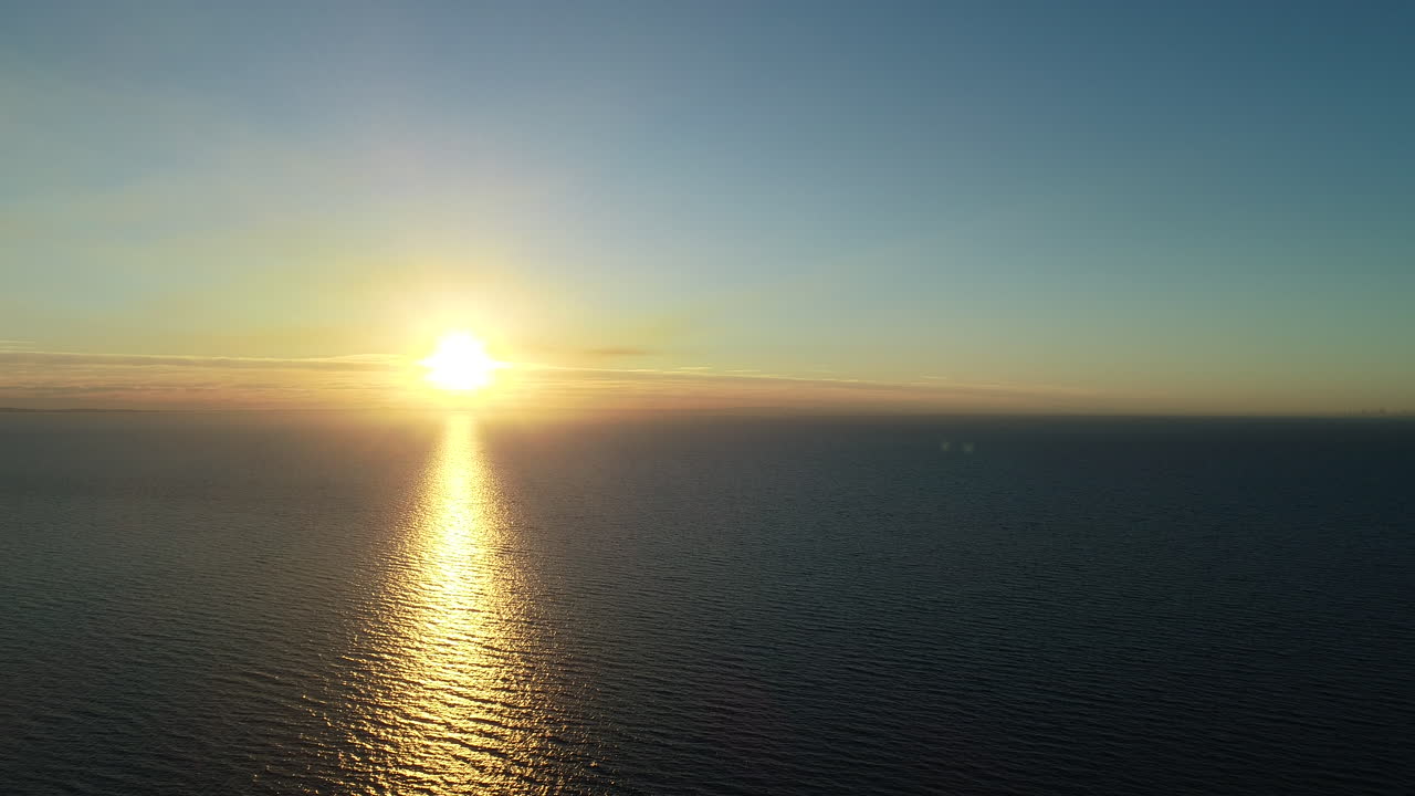 Glowing sunset over large ocean body of water from aerial perspective.