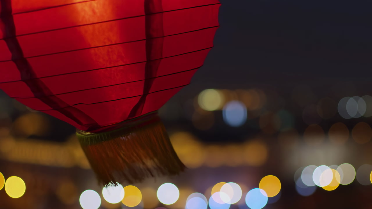 Red Paper Lantern With City Bokeh And Warm Glow, Tassel Detail Swings Above Blurred Skyline, Cozy Evening