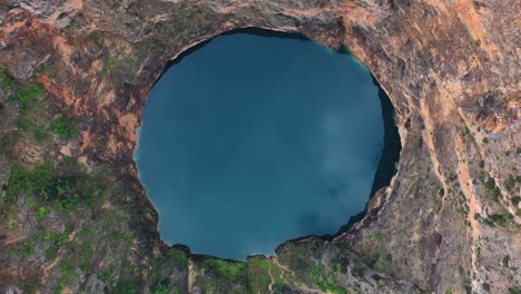 Aerial-top-down-view-of-blue-water-lake-formed-in-deep-sinkhole-completely-surrounded-by-tall-cliffs-in-Imotski,-Croatia