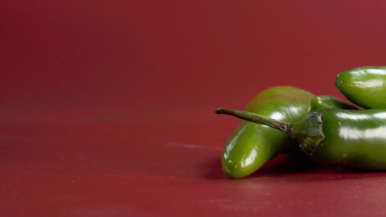 Makronærbilde av friske grønne jalapeño-paprika arrangert på rød bakgrunn. Glatt, blankt skinn, levende farge og buede former skaper en ren matkomposisjon med plass til tekst.