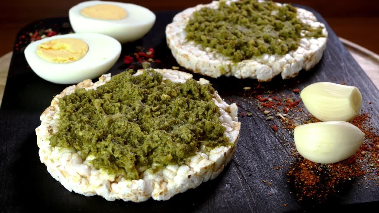las tostadas de pastel de arroz con salsa de pesto verde y huevos hervidos giran lentamente en la tabla de cortar.