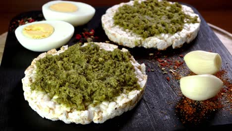 las tostadas de pastel de arroz con salsa de pesto verde y huevos hervidos giran lentamente en la tabla de cortar.