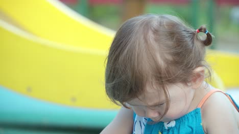 Niña-Pequeña-Disgustada-Sentada-En-El-Suelo-En-Un-Patio-De-Recreo-Al-Aire-Libre-Con-La-Cabeza-Inclinada