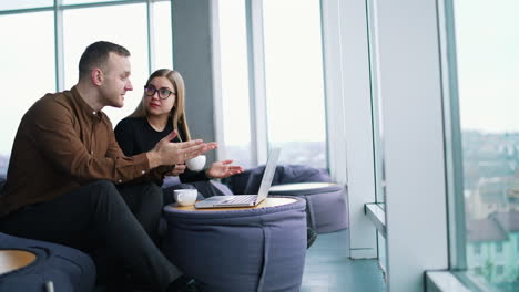 young business people talk in modern office. handsome businessman and female partner sitting in comfortable chairs and having a conversation in front of a laptop.