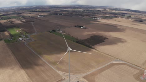 Inclinación-Lenta-Hacia-Arriba-Que-Revela-Vastas-Tierras-De-Cultivo-Alrededor-De-Una-Turbina-Eólica