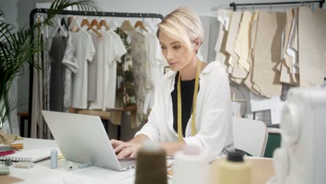 woman tailor sitting at the table using laptop in workshop