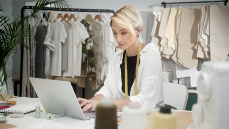 mujer sastre sentada en la mesa usando una laptop en el taller