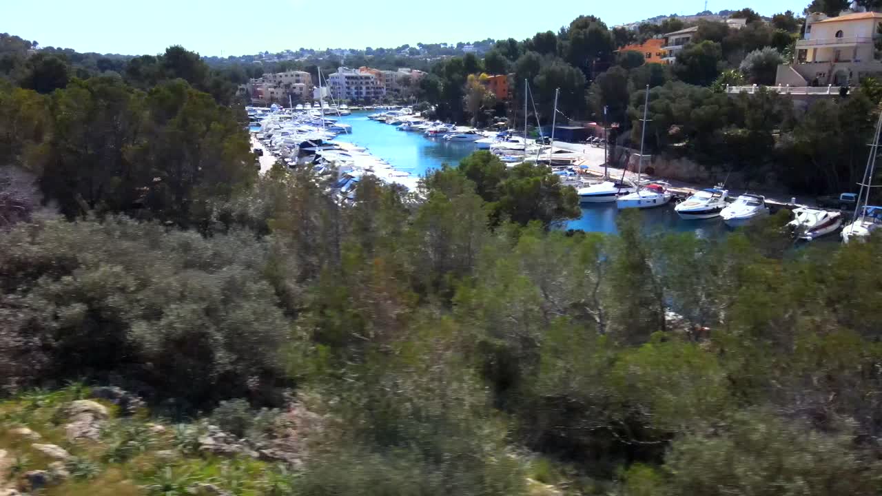 Experience the stunning marina of Santa Ponsa in Mallorca with boats docked peacefully and vibrant blue waters. The beautiful coastal scenery is complemented by clear skies and lush surroundings.