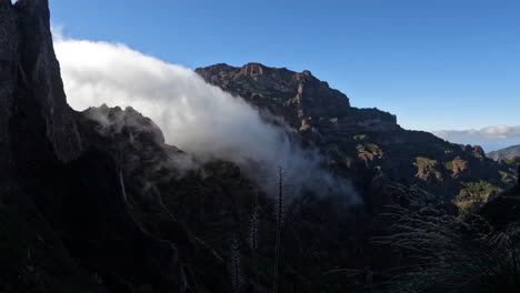 The-drone-captures-a-mesmerizing-scene-as-clouds-gracefully-flow-through-the-mountainous-terrain,-creating-a-dynamic-and-ethereal-spectacle-of-nature's-beauty-in-motion