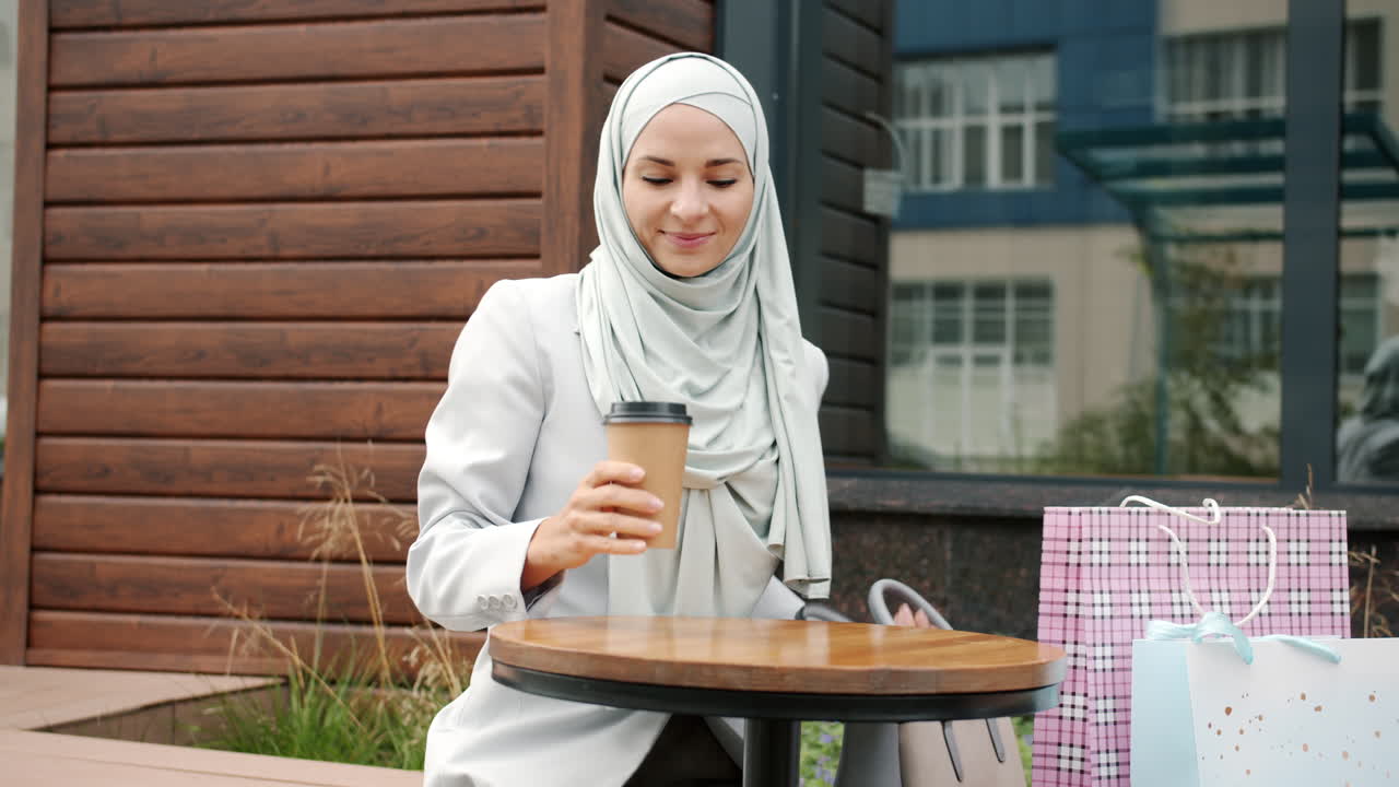 Woman enjoying coffee and shopping bags at an outdoor cafe.