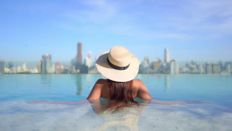 인피니티 옥상 수영장에서 현대적인 도시 경관을 배경으로 멋진 전망을 감상할 수 있는 세련된 여성의 뒷모습
