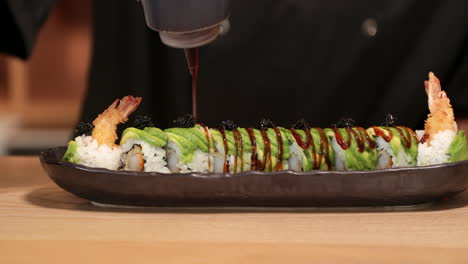 chef experto poniendo salsa encima de los rollos de sushi antes de servir.
