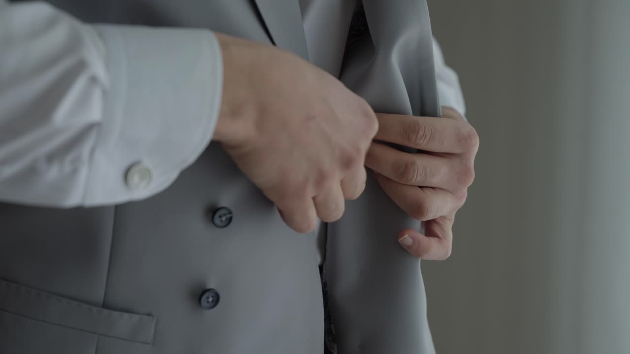 Close up tangan sedang mengancingkan kancing pada rompi jas abu-abu