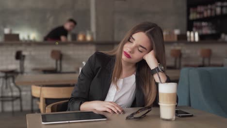 an exhausted businesswoman sits in a café with her devices and a cup of coffee on the table