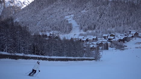 A-woman-descends-a-ski-slope-by-making-turns,-piste-in-the-Swiss-Alps-next-to-a-forest,-winter-sport