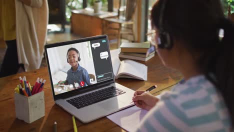 Schoolgirl-using-laptop-for-online-lesson-at-home,-with-her-colleague-and-web-chat-on-screen